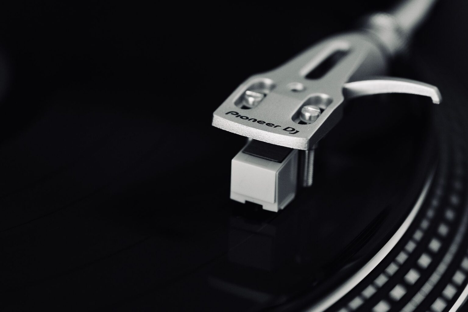 Czarno-białe zbliżenie na ramię gramofonu z wkładką Pioneer DJ odtwarzającego klasyczną płytę winylową