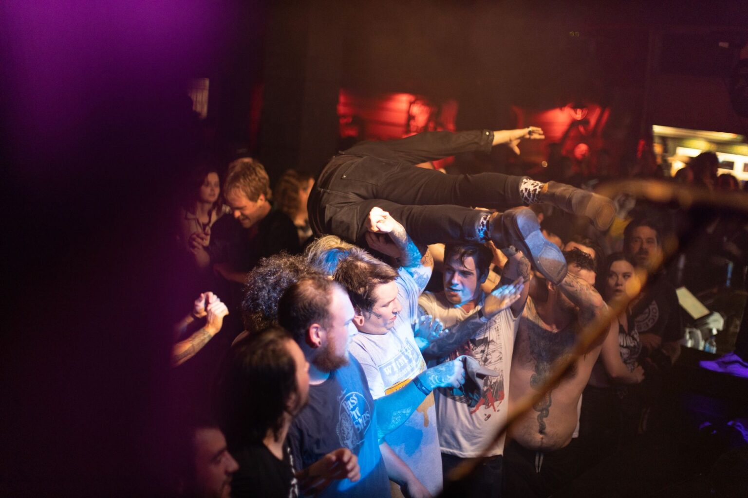 Tłum ludzi na koncercie hardcore podtrzymuje unoszonego w górę, skaczącego na publiczność muzyka