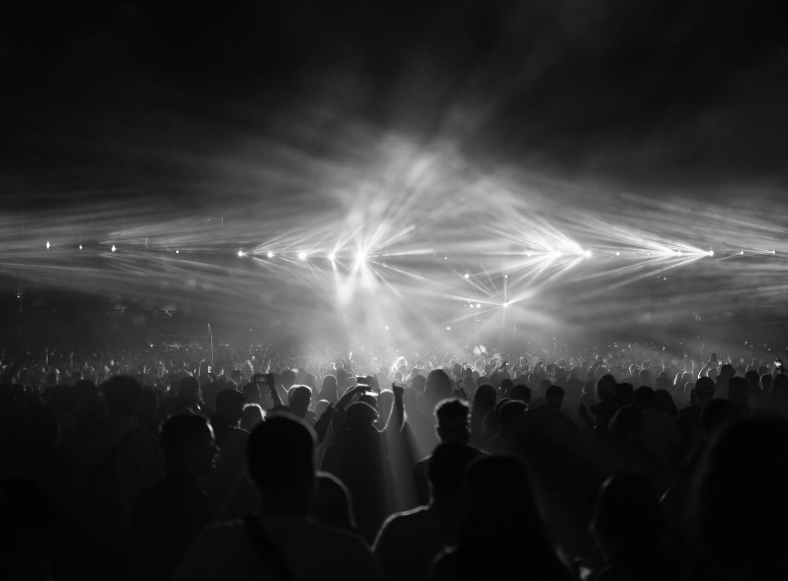 Czarno-biały tłum ludzi bawiących się na gigantycznym festiwalu muzycznym w blasku reflektorów