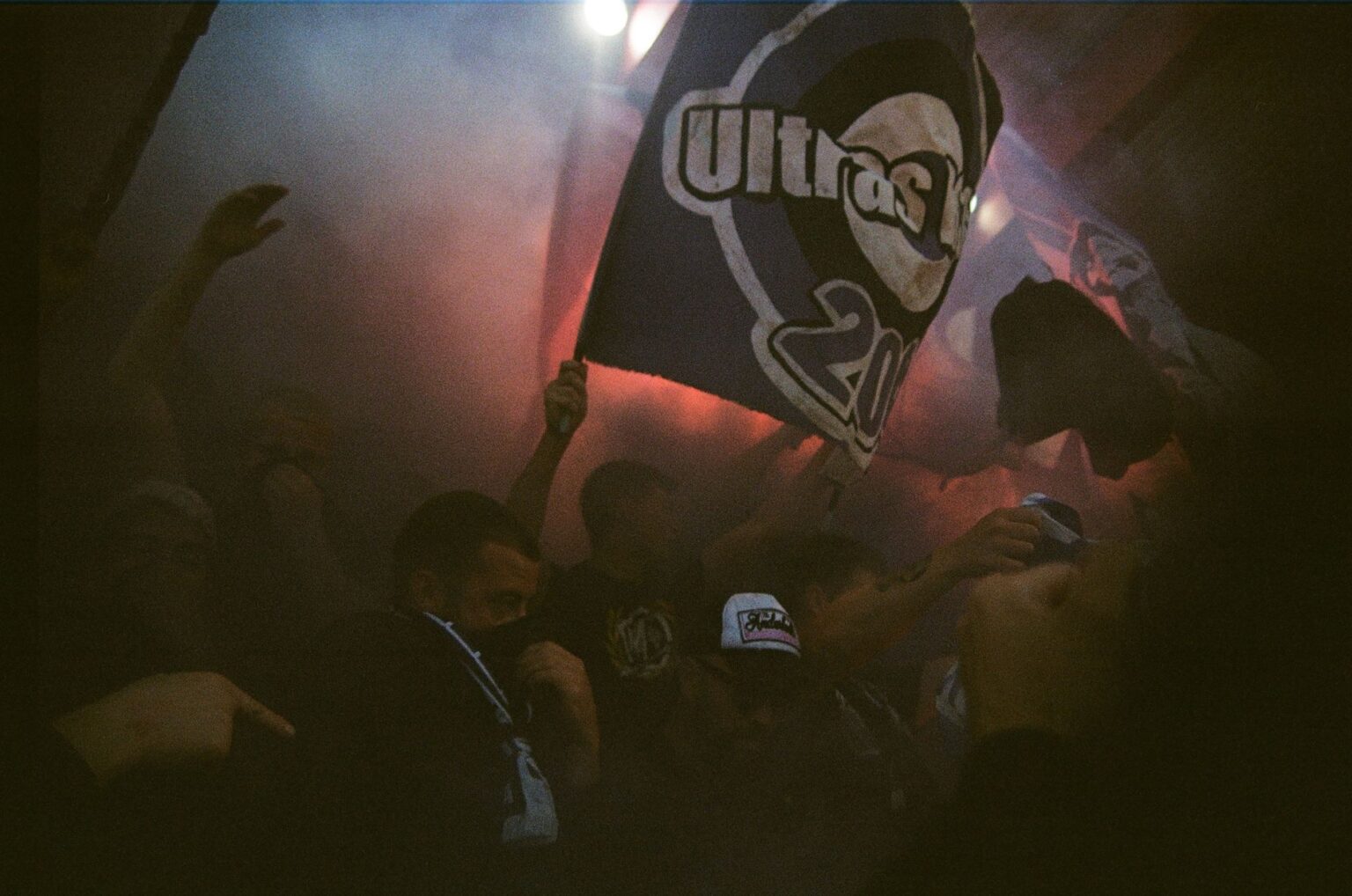 Najciekawsze eventy hardcore w Europie – przewodnik dla fanów Tłum ludzi macha flagą z napisem Ultras w dymie i czerwonym świetle na europejskim evencie hardcore