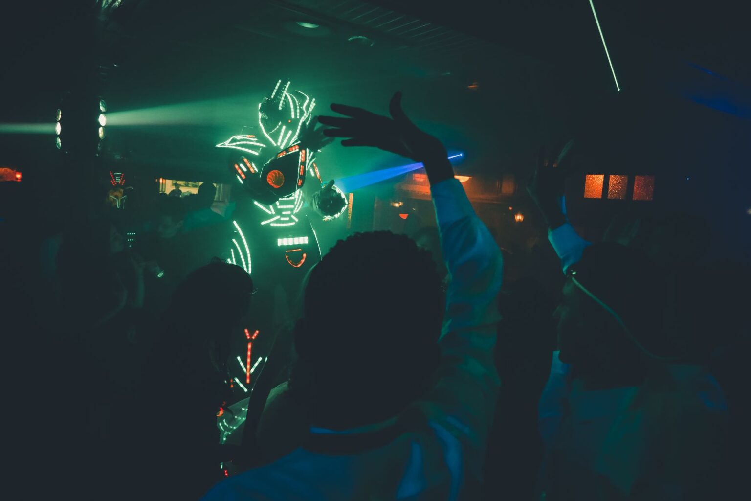 Tłum na ciemnym parkiecie klubu tańczy przed postacią w świecącym na zielono stroju hardstyle