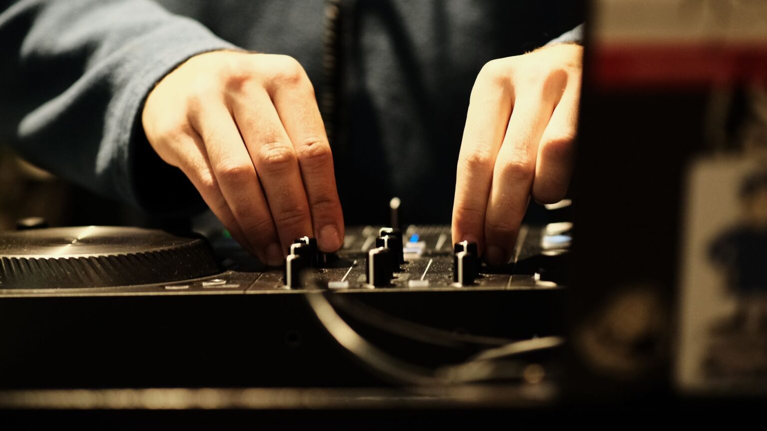 Zbliżenie na dłonie DJ-a obsługujące pokrętła i suwaki na nowoczesnym kontrolerze DJ-skim