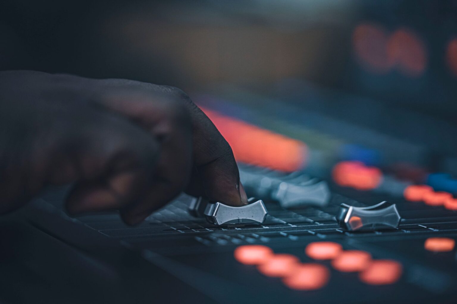 Ręka sounddesignera przesuwa suwak na profesjonalnym mikserze audio podczas pracy nad dźwiękiem