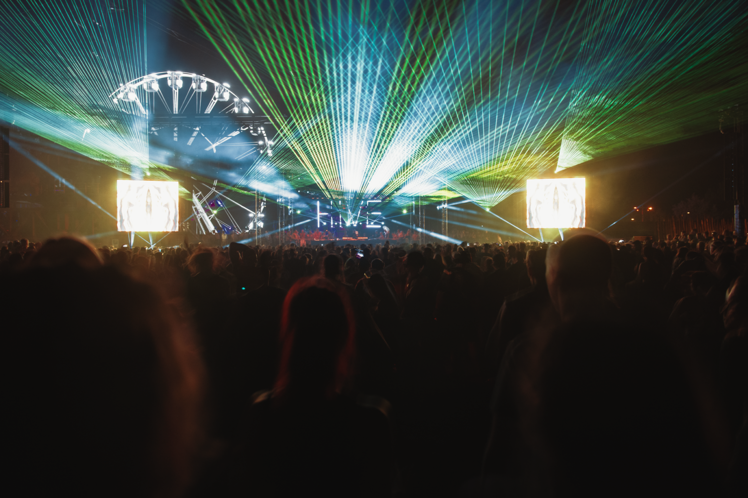 Nocny tłum na festiwalu muzyki elektronicznej pod pokazem zielonych laserów i świateł